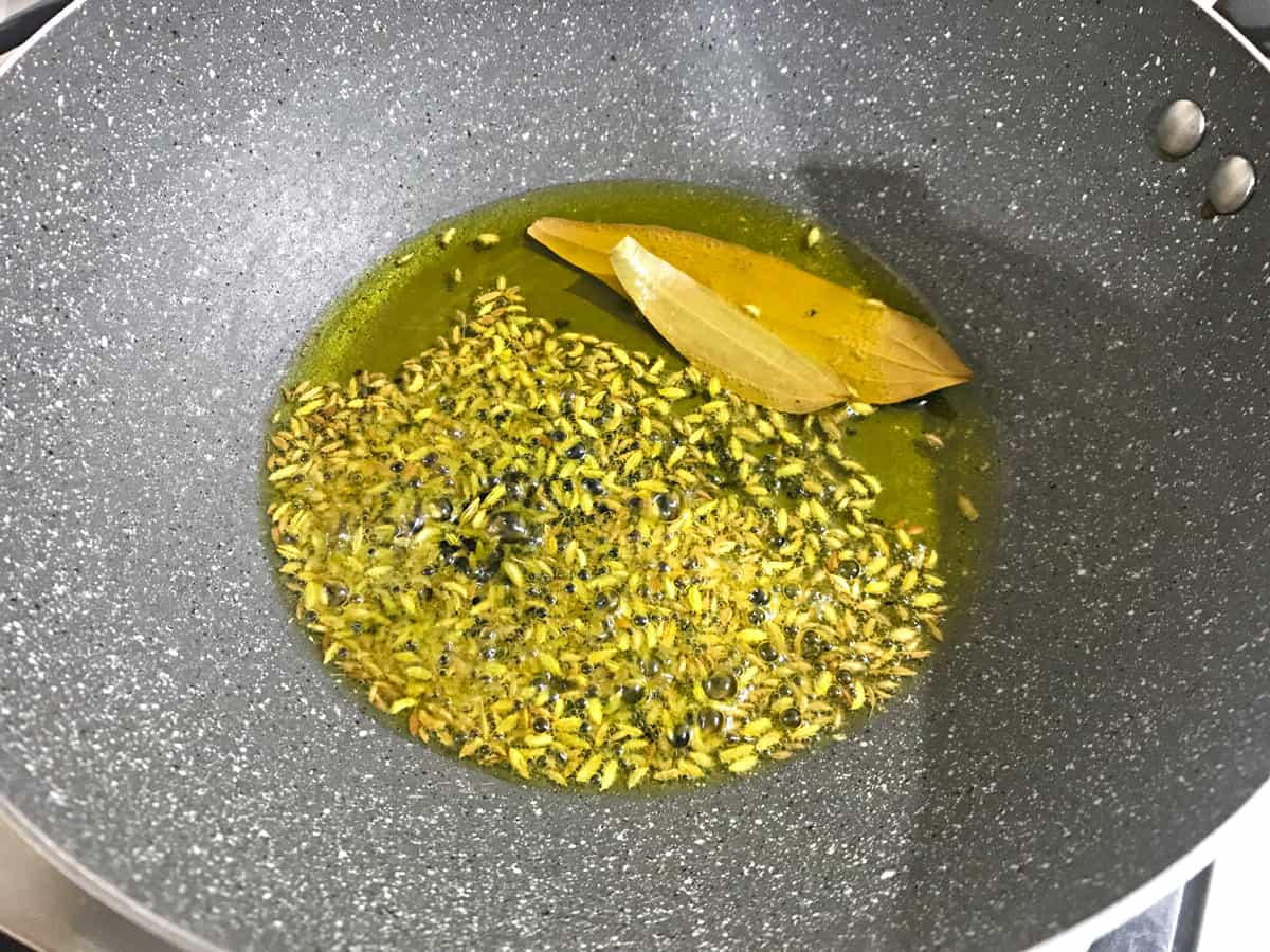 Cumin, fennel, fenugreek, nigella seeds, asafoetida and bay leaves frying in hot mustard oil in pan.