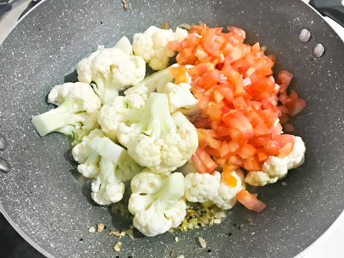Cauliflower florets and chopped tomatoes added to the pan.