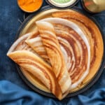 four plain dosa folded and served on a brass platter with coconut chutney in bowl on side.