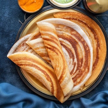 four plain dosa folded and served on a brass platter with coconut chutney in bowl on side.