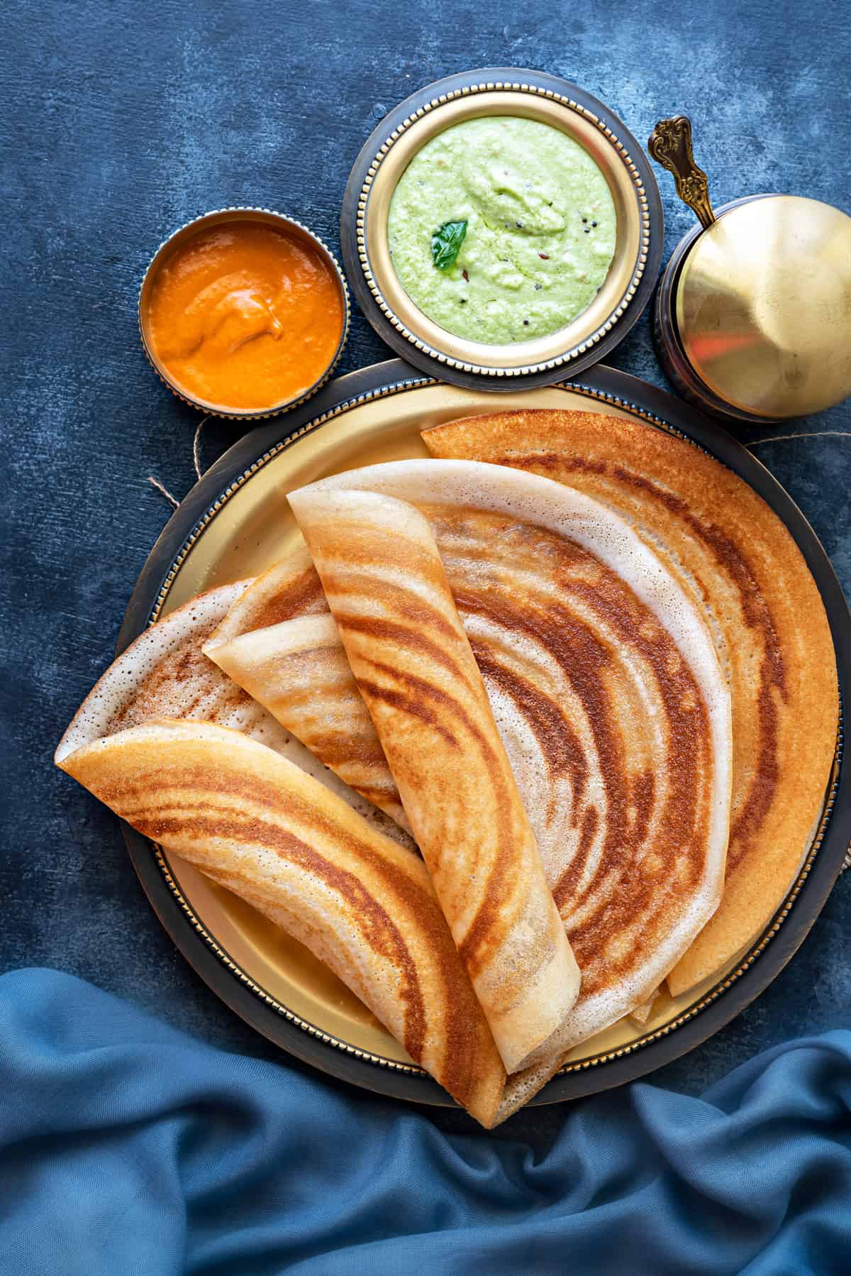 Four plain dosa folded and served on a brass platter with tomato and coconut chutney in bowl on side.