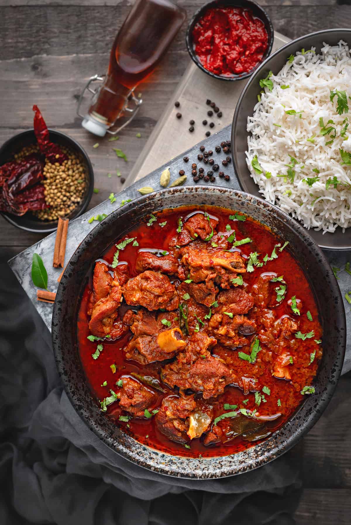 Overhead view of a black bowl with lamb vindaloo curry, served with a bowl of rice on side.