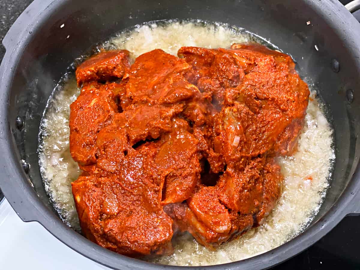 marinated lamb pieces frying in the traditional pressure cooker on the stovetop.