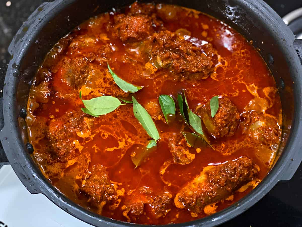 Adding curry leaves and water to the pressure cooker.