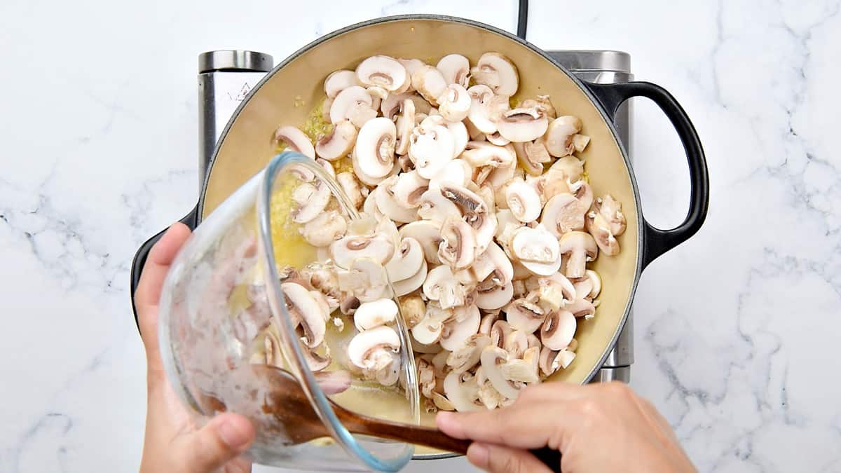 hands putting sliced mushrooms into the pot.