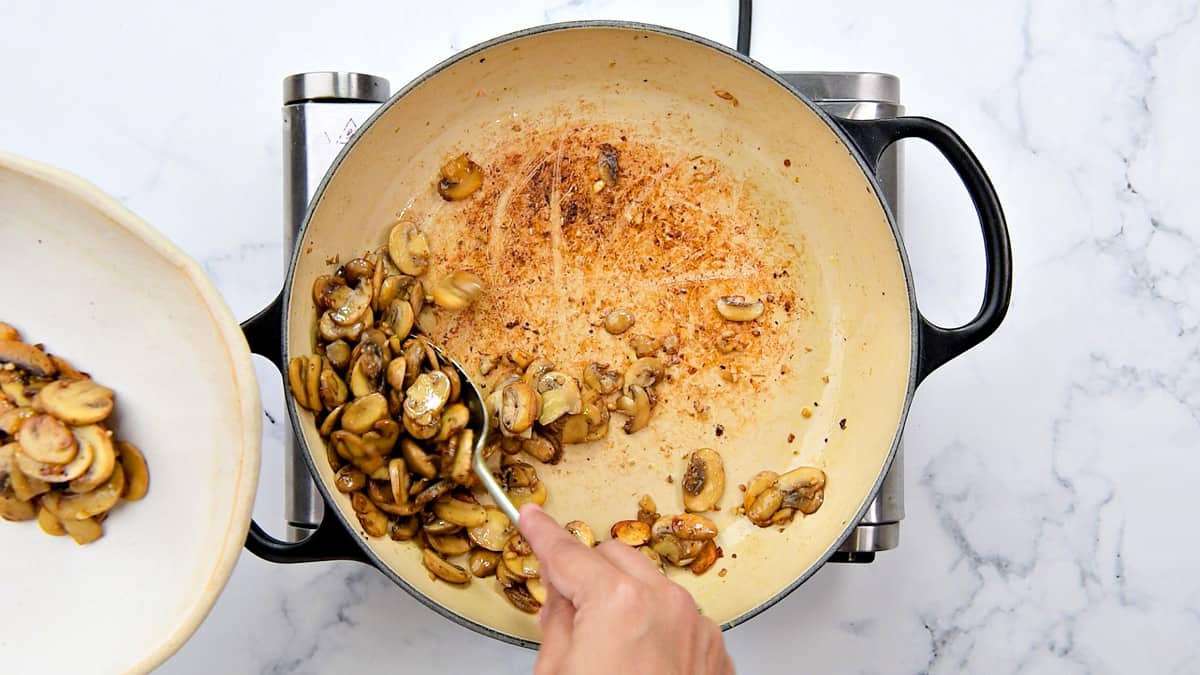 Spooning mushrooms out of the pot and into a bowl.