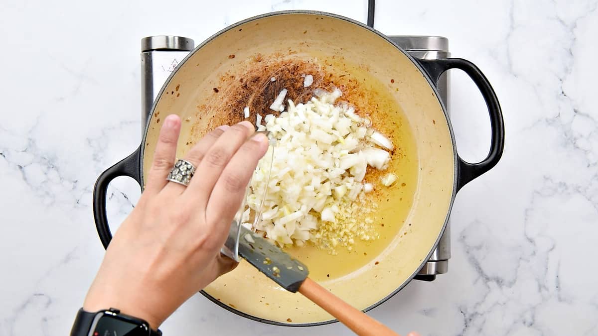 Hand adding white minced onion to the pot with a spatula.
