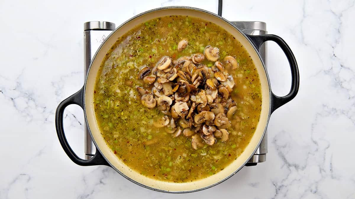 Adding broth and sautéed brown mushrooms in the pot.