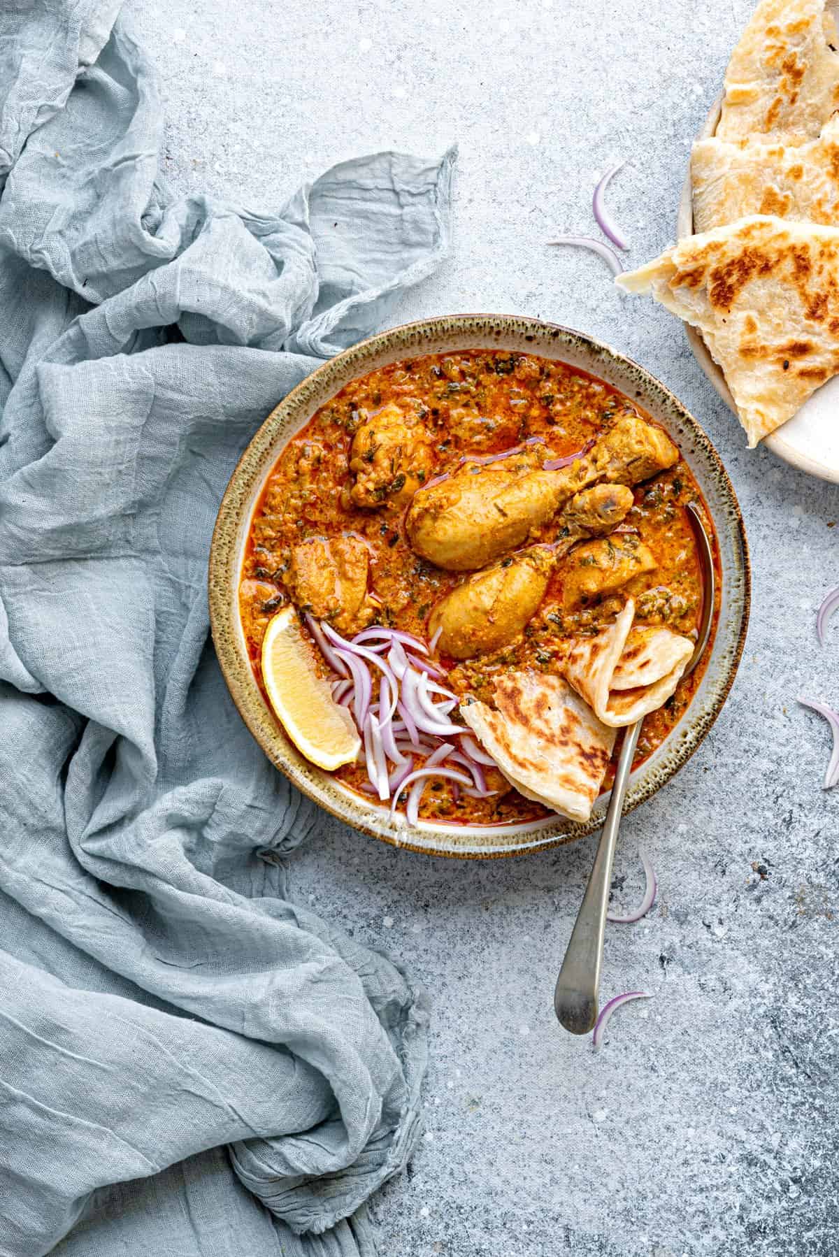 Fenugreek chicken curry in ceramic bowl with a spoon and a piece of paratha into it.