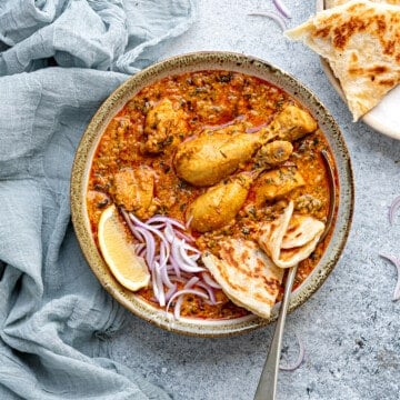 Fresh methi chicken curry served in earthen bowl, parathas on side.