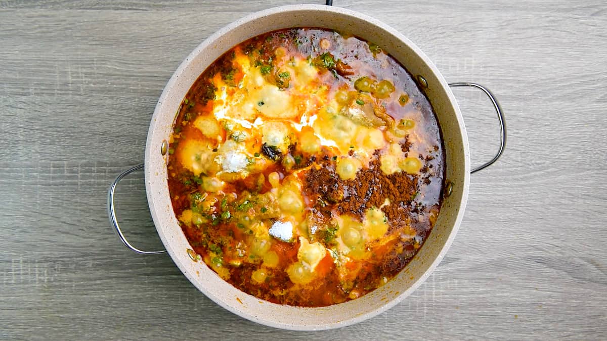 Cream, garam masala powder, and sugar added to the chicken methi curry cooking in the pot.