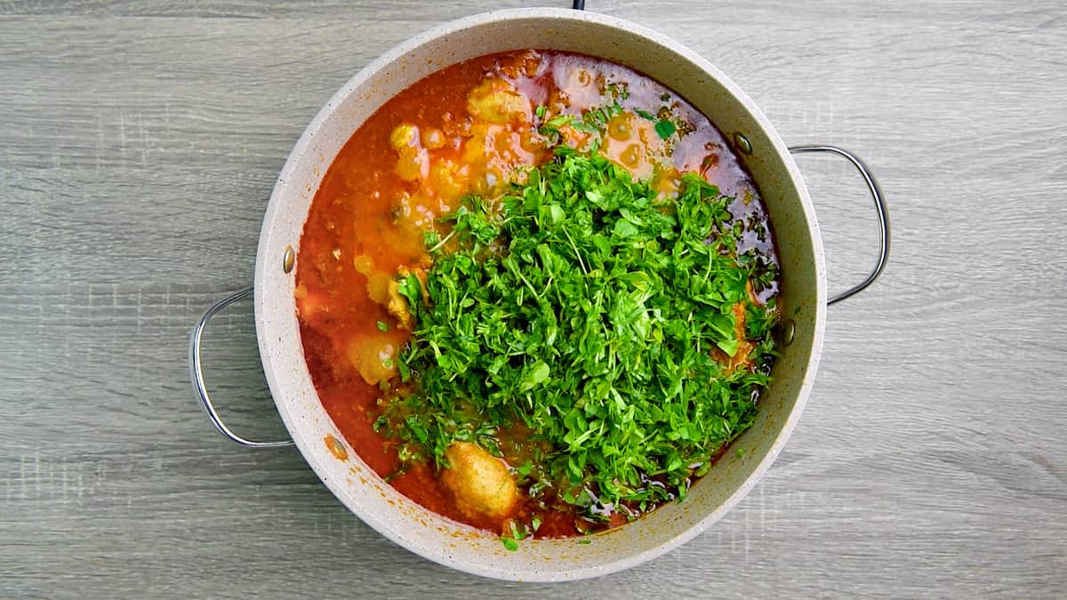 Chopped fresh fenugreek leaves and lemon juice added to chicken curry cooking in the pot.