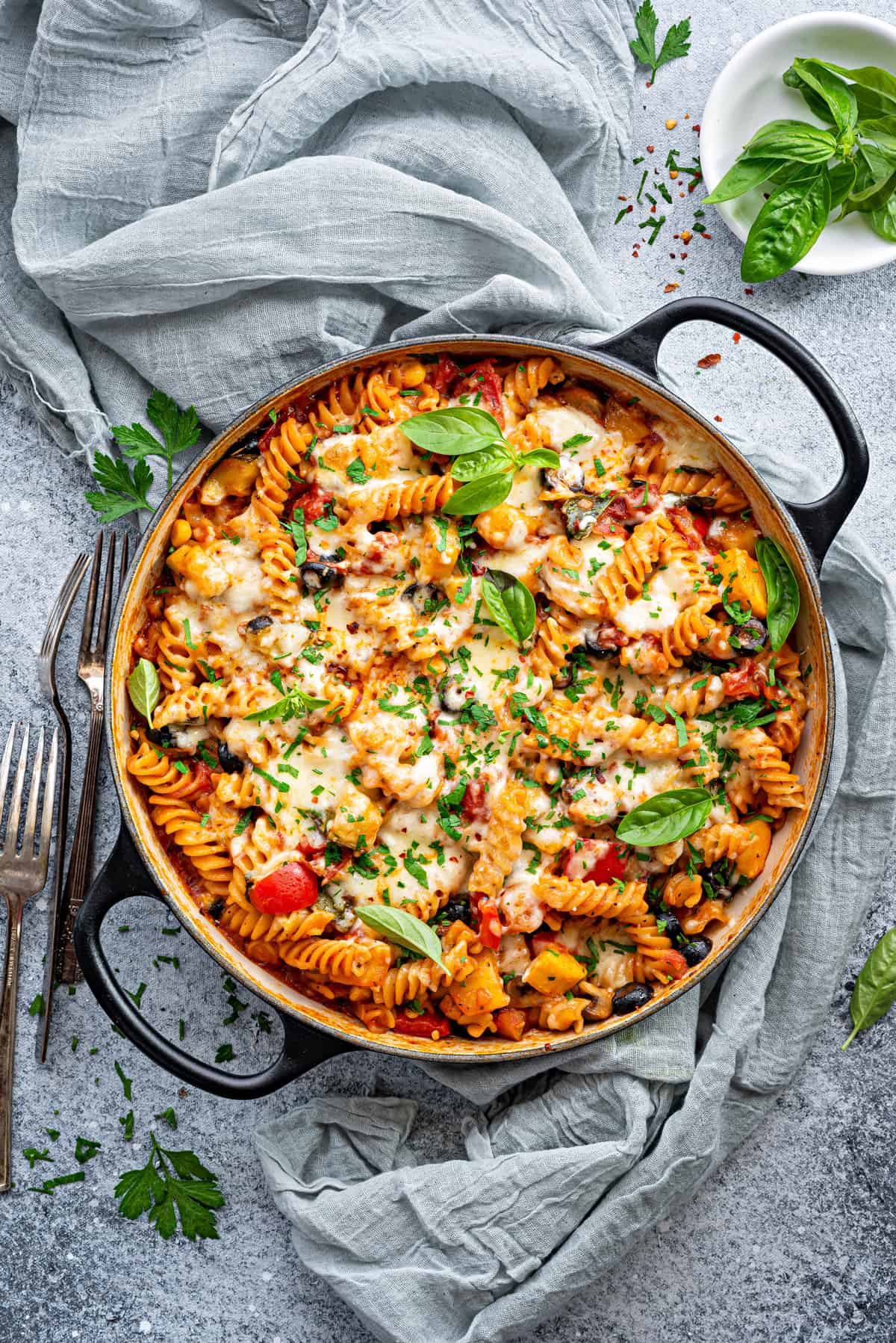 Close-up of mixed vegetable pasta in a pot garnished with fresh basil and parsley.