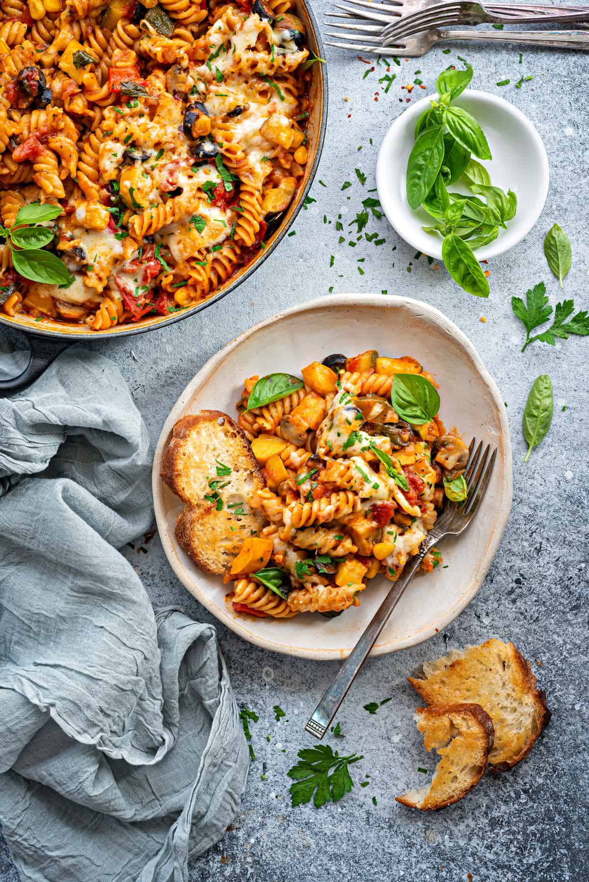 A serving portion of vegetable pasta on a ceramic plate with toasted sourdough and a fork.