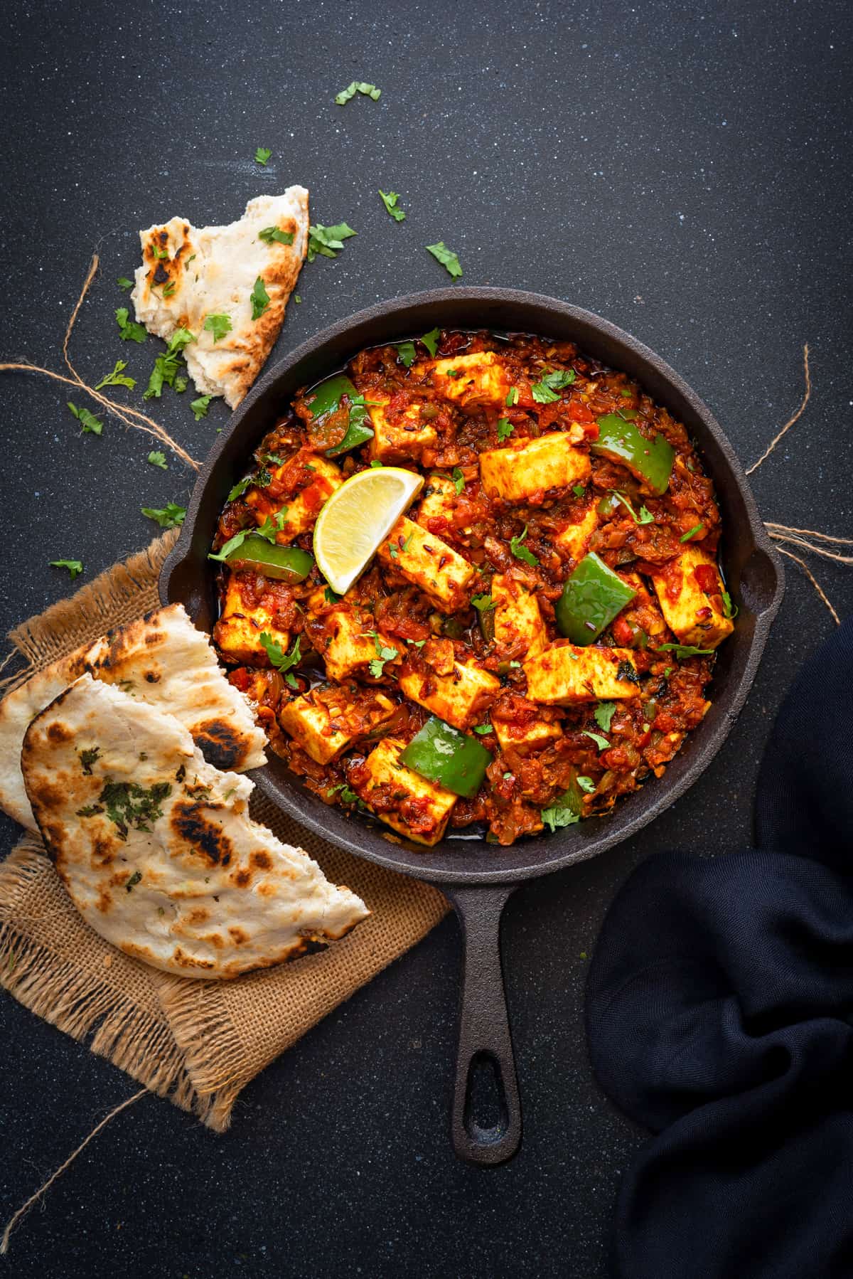 Tawa Paneer masala curry served iron skillet with two pieces of naan on side.