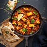 Tawa Paneer masala curry served iron skillet with two pieces of naan on side.