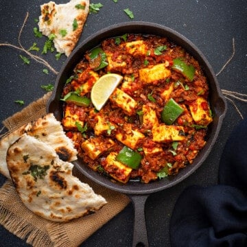 Tawa Paneer masala curry served iron skillet with two pieces of naan on side.