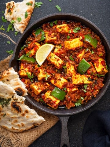 Tawa Paneer masala curry served iron skillet with two pieces of naan on side.