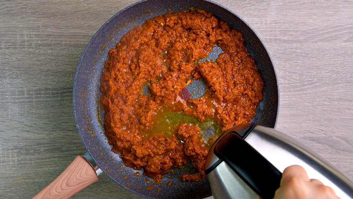 Adding around five tablespoons of warm water to masala base in the skillet.