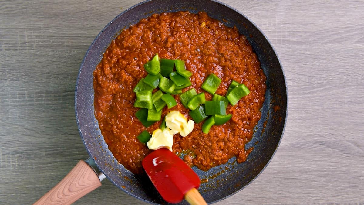 Diced capsicum and butter added to the tawa masala cooking  in the skillet.