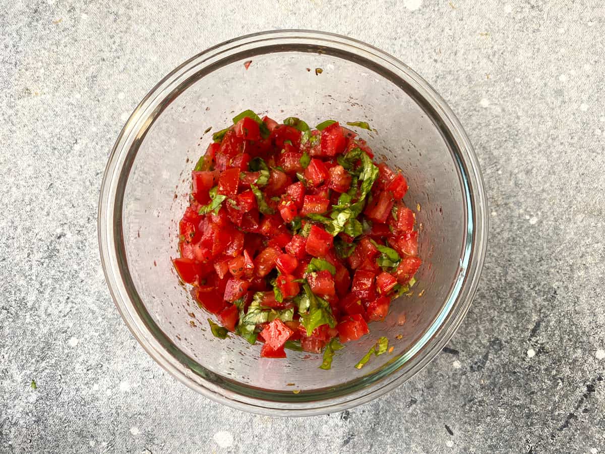 Combined mixture in a glass bowl with chopped tomatoes, sliced basil, olive oil, and spices.
