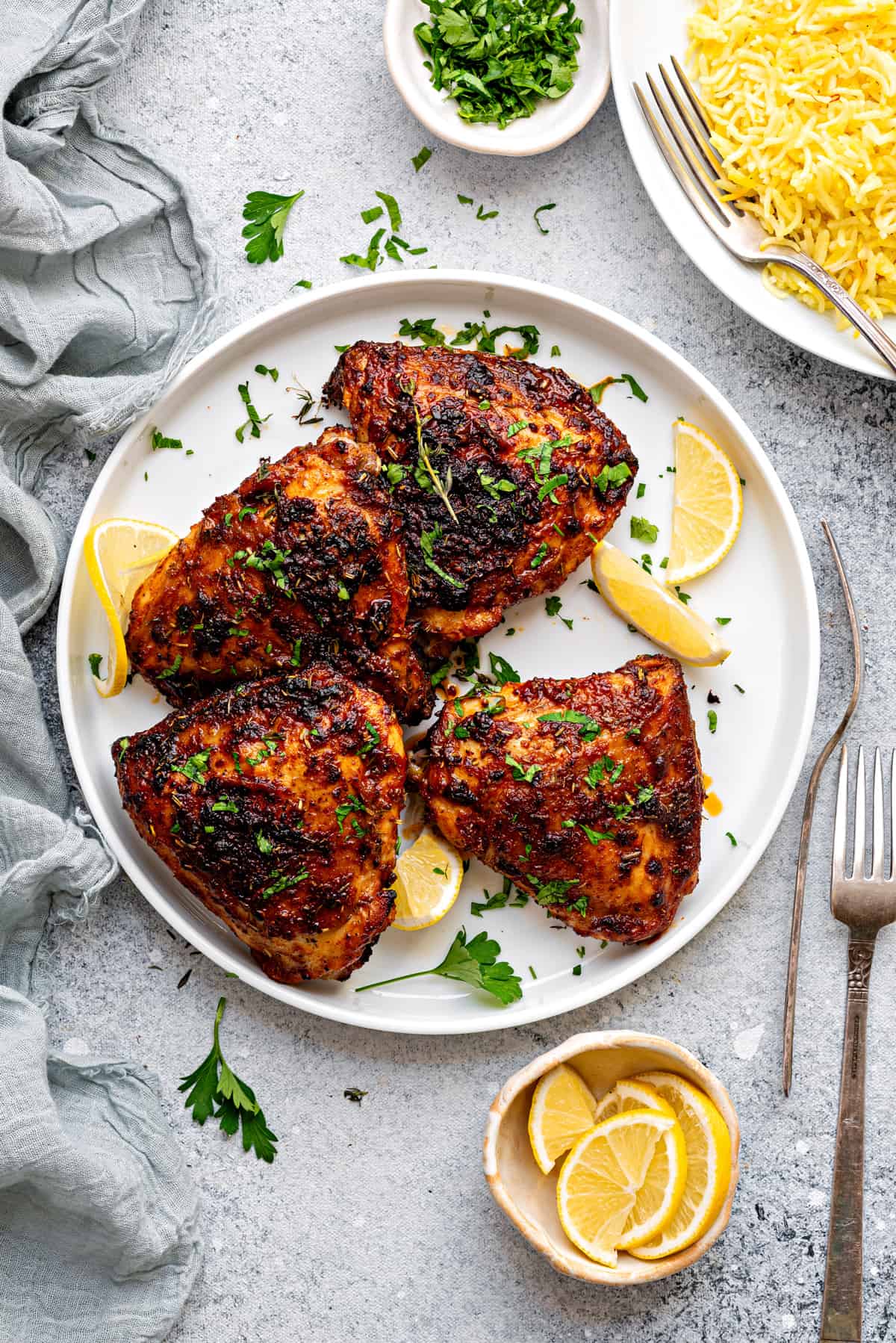 Four air fried chicken thighs on a white plate garnished with fresh parsley and lemon slices.