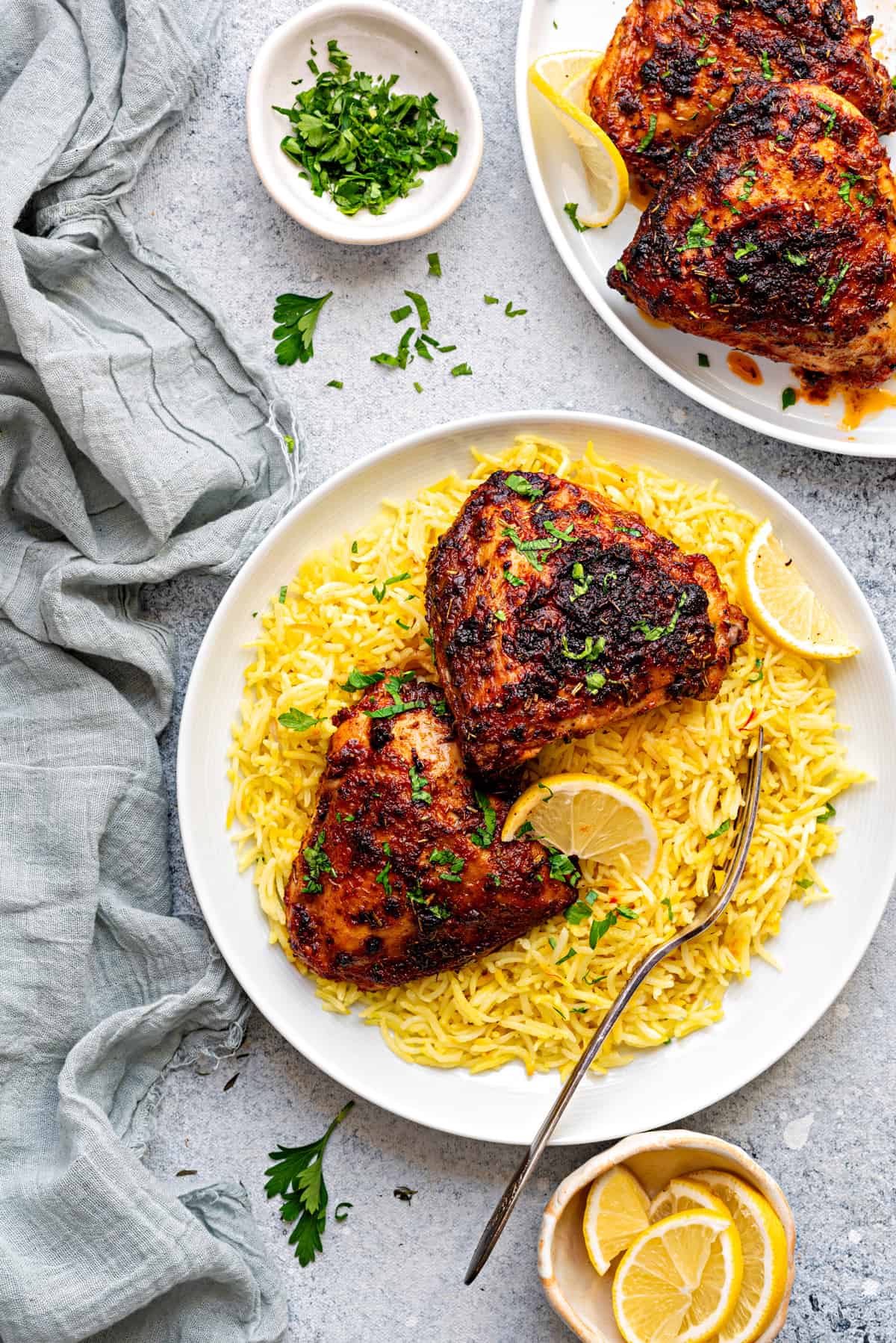 Two air fryer bone-in and skin-on chicken thighs on a white plate, served on top of yellow saffron rice.