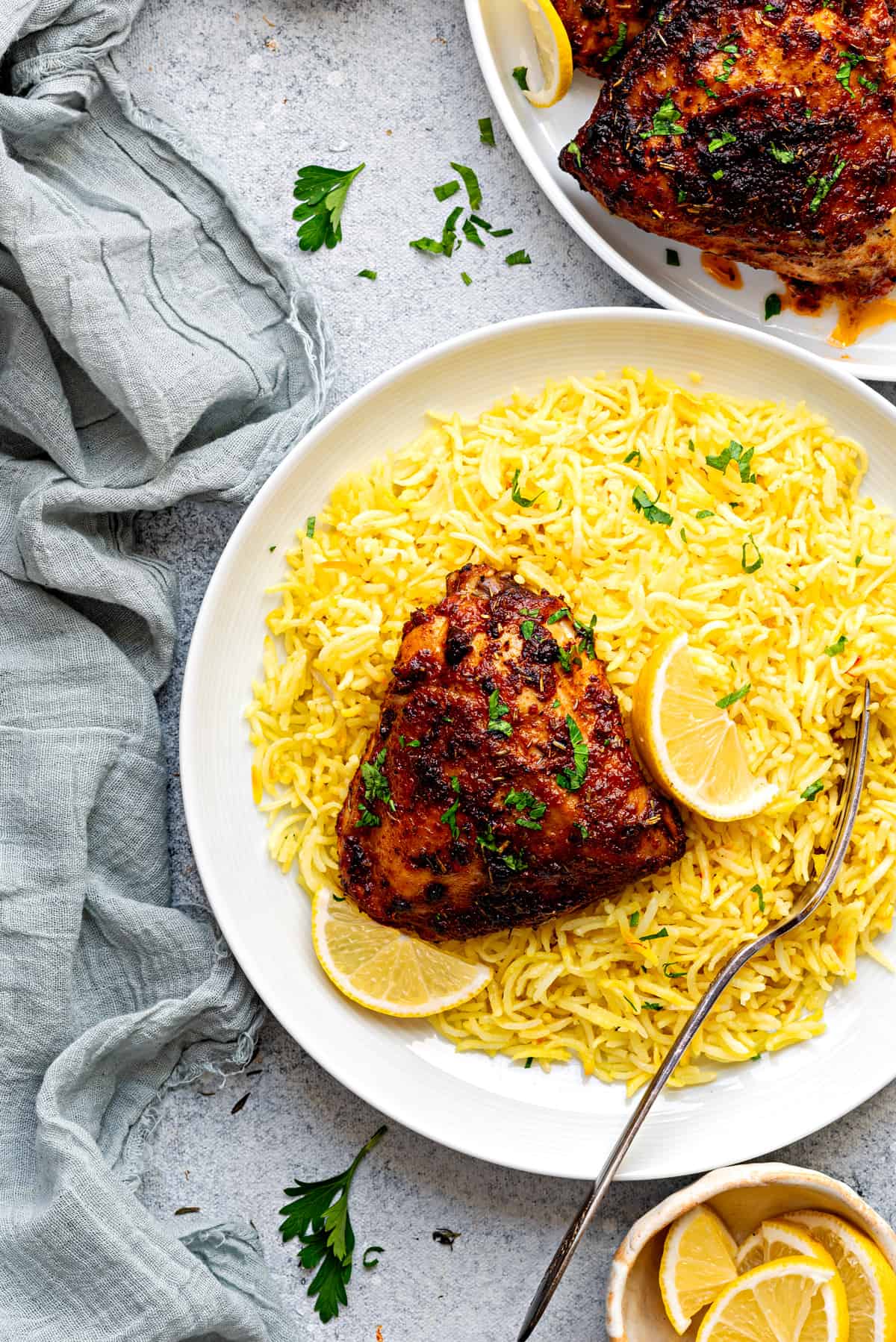 One air fryer bone-in chicken thigh on a white plate, nestled on top of yellow saffron rice.