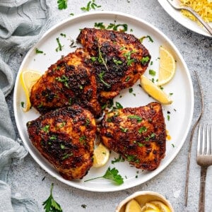 Four air fried chicken thighs on a white plate garnished with fresh parsley and lemon slices.