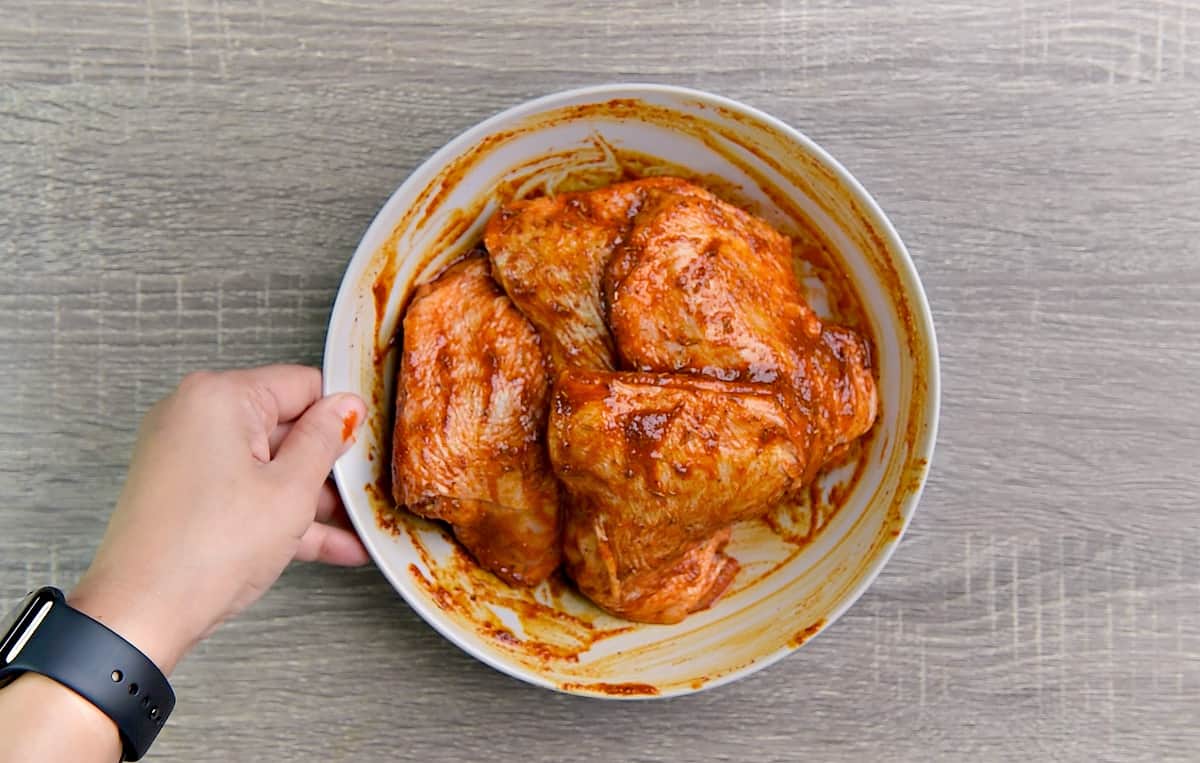 Four raw chicken thighs in bowl. All are coated in the marinade.