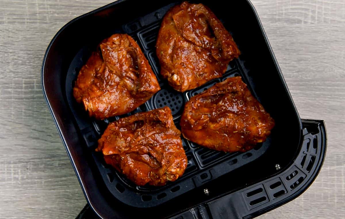 Four bone-in marinated chicken thighs placed in an air fryer basket with skin side down.