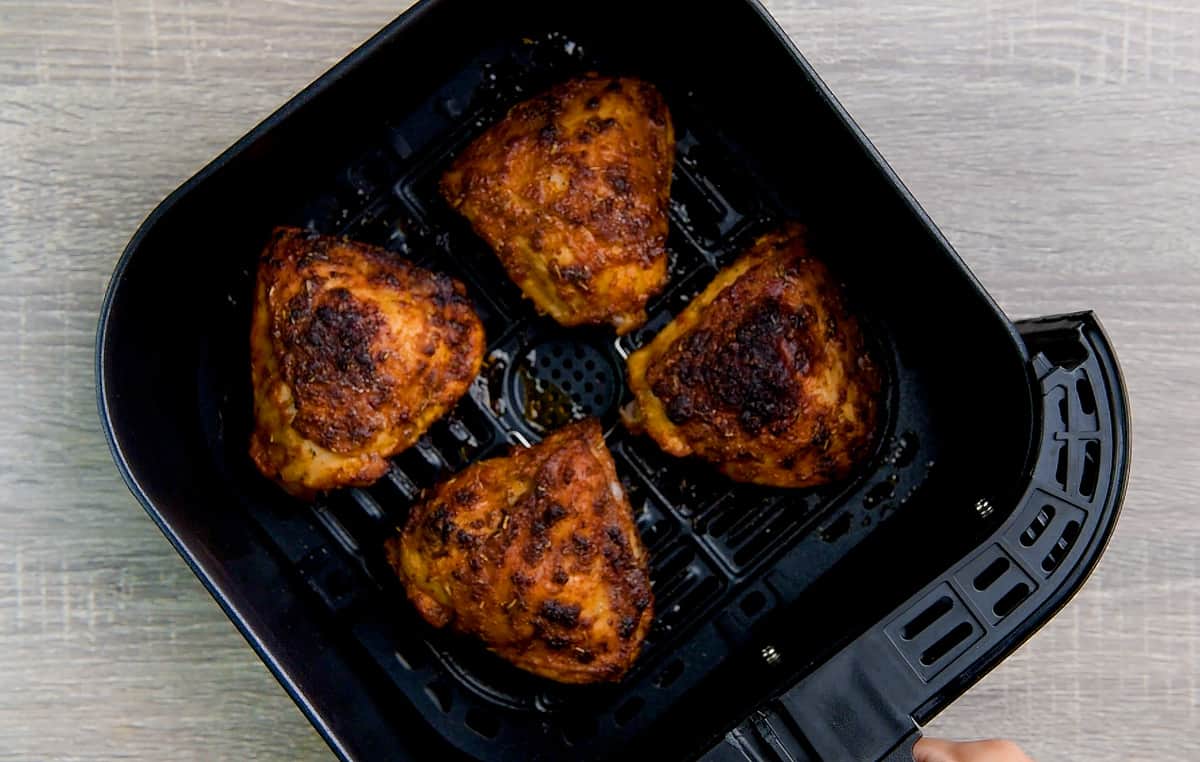 Four skin-on bone-in marinated chicken thighs in an air fryer basket.
