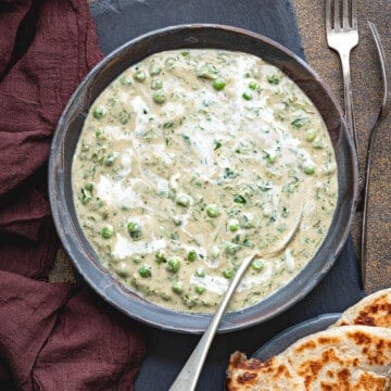 Close-up of methi matar malai curry served in black bowl with a spoon.