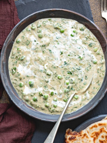 Close-up of methi matar malai curry served in black bowl with a spoon.