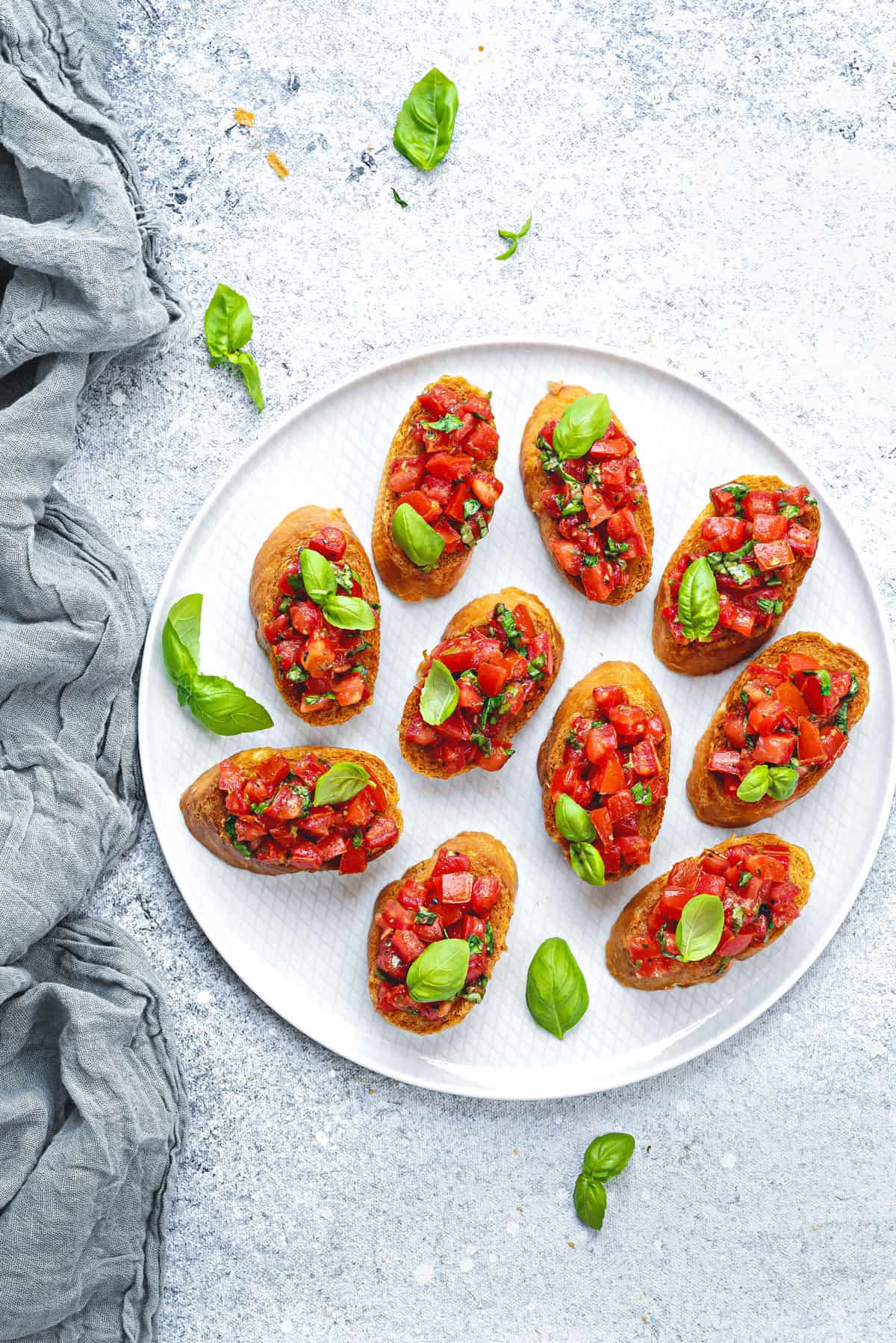 Top down view of a white plate with 10 servings of bruschetta. A few pieces of baby basil garnish the plate.