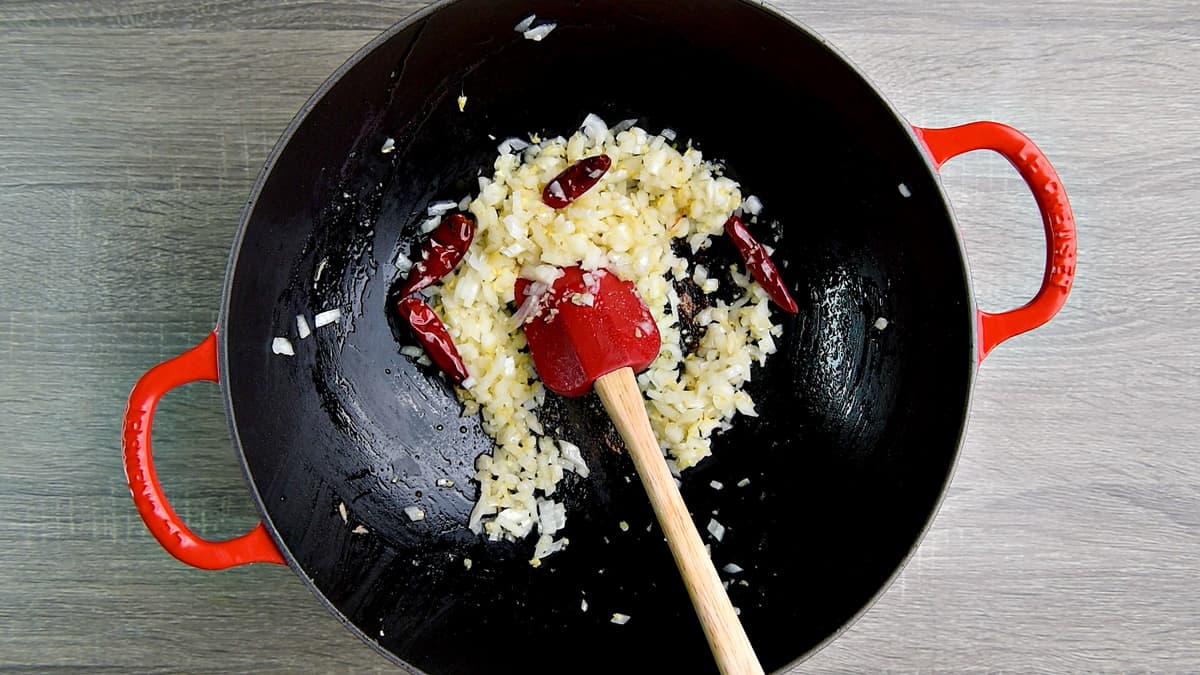 Using a red spatula to stir fry garlic, ginger and onion in a wok.