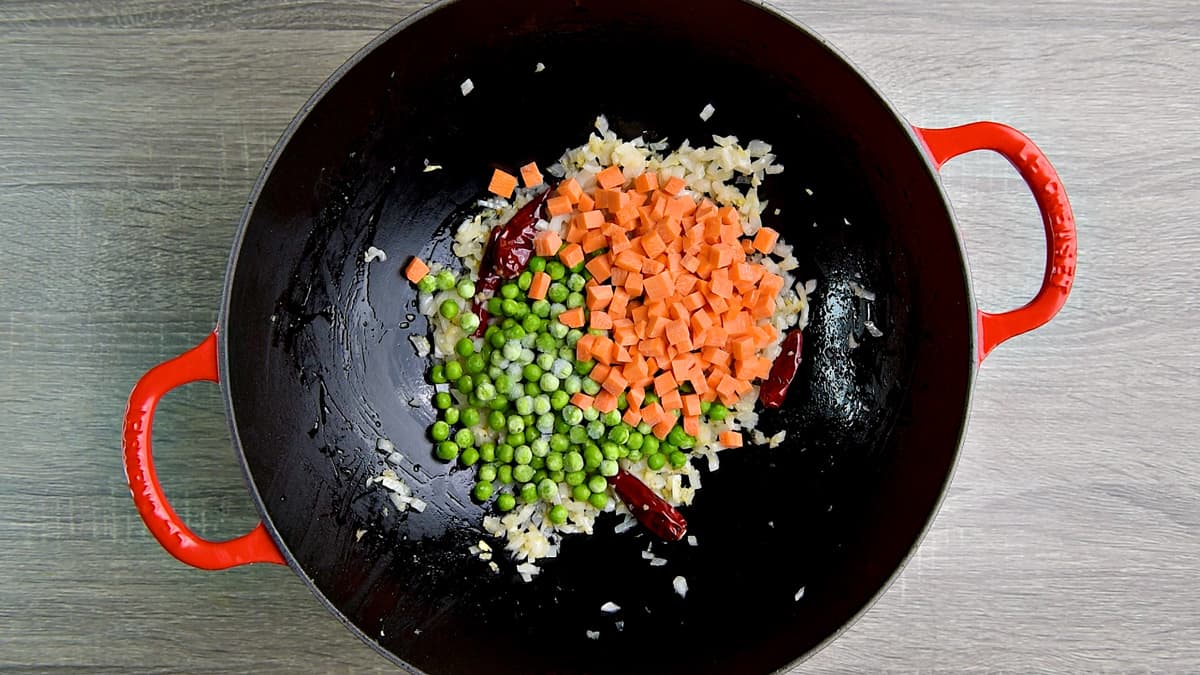 Chopped carrots, peas, and aromatics in a wok.