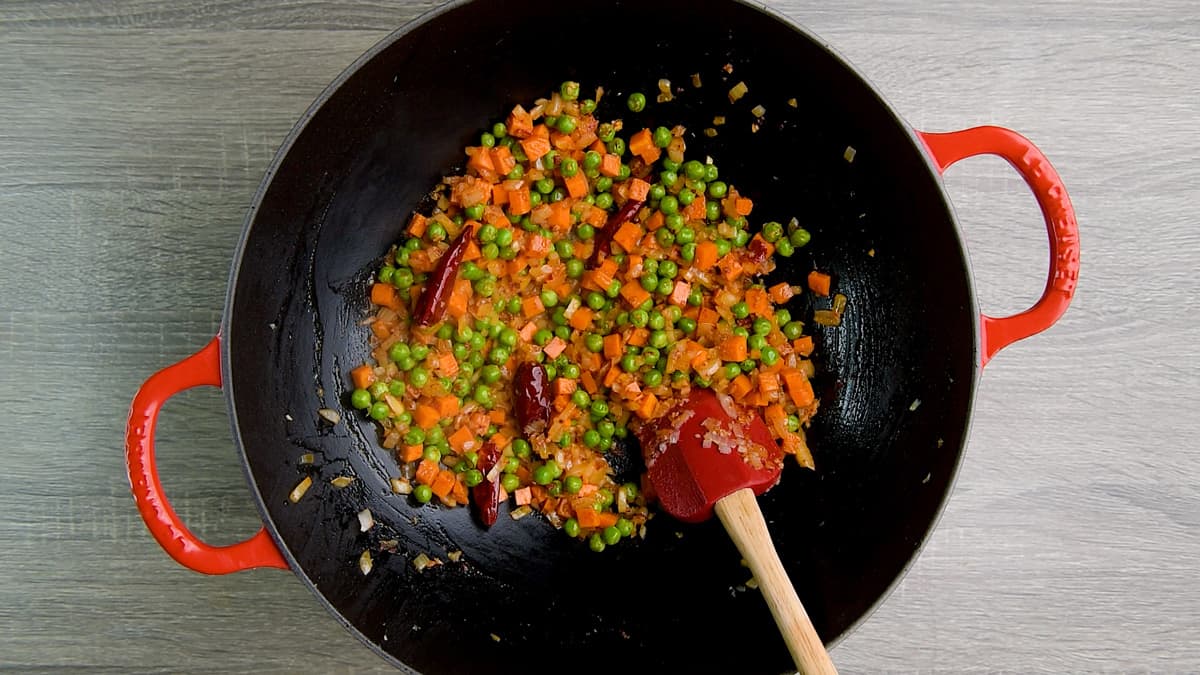 Stir frying carrots and peas with salt, pepper, chili paste and vinegar in a wok.