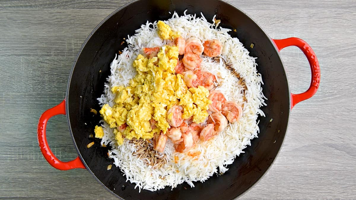 White cooked rice, dark soy sauce, cooked shrimp, and scrambled eggs in a wok.