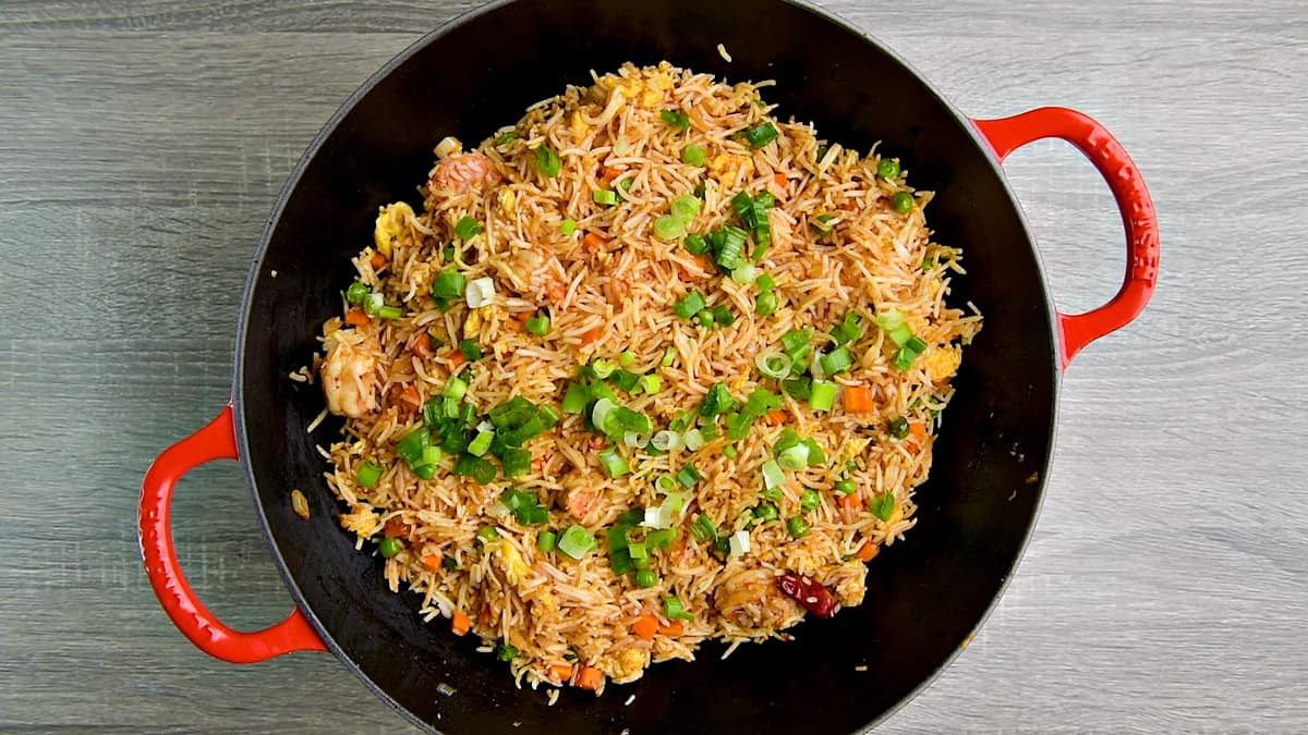 Garnishing wok of shrimp fried rice with sesame oil, and sliced green scallions.