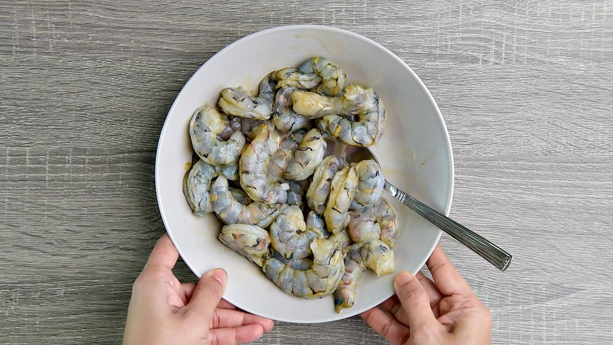 Raw shrimp in a white bowl, tossed with spices.