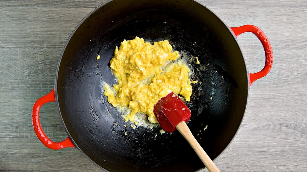 Making scrambled eggs in a wok with red spatula.