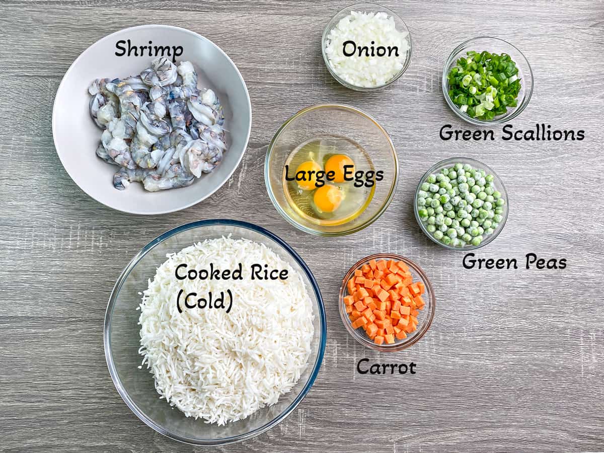 Recipe ingredients in individual glass dishes - green peas, carrot, shrimp, rice, eggs, onion and scallions.