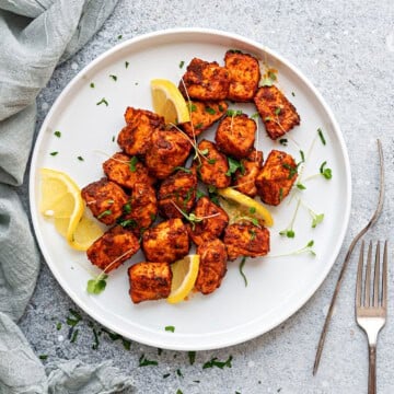 White plate with serving of salmon bites, with slices of lemon tucked in.