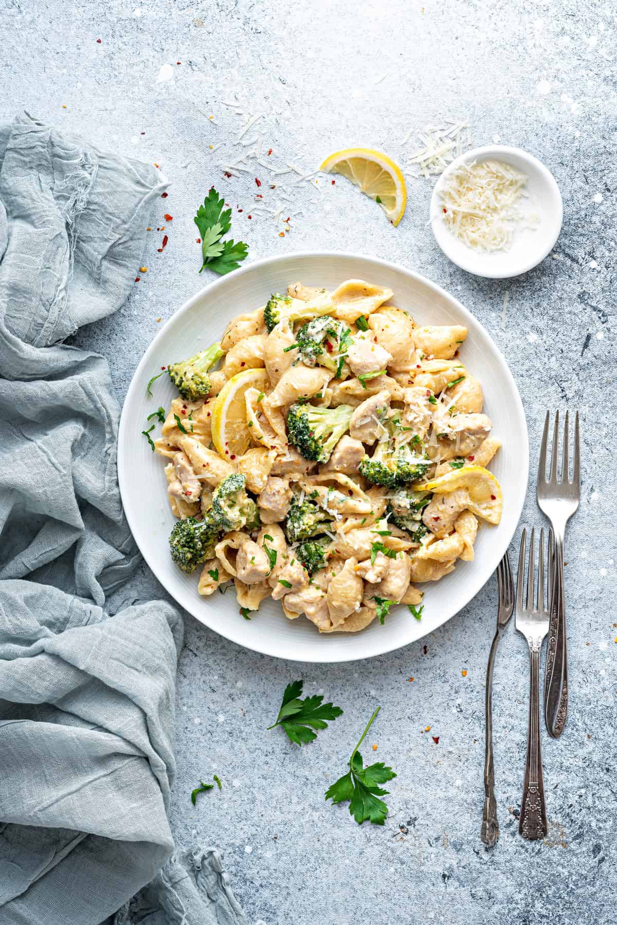 White plate of chicken broccoli pasta. Two forks are to the side.