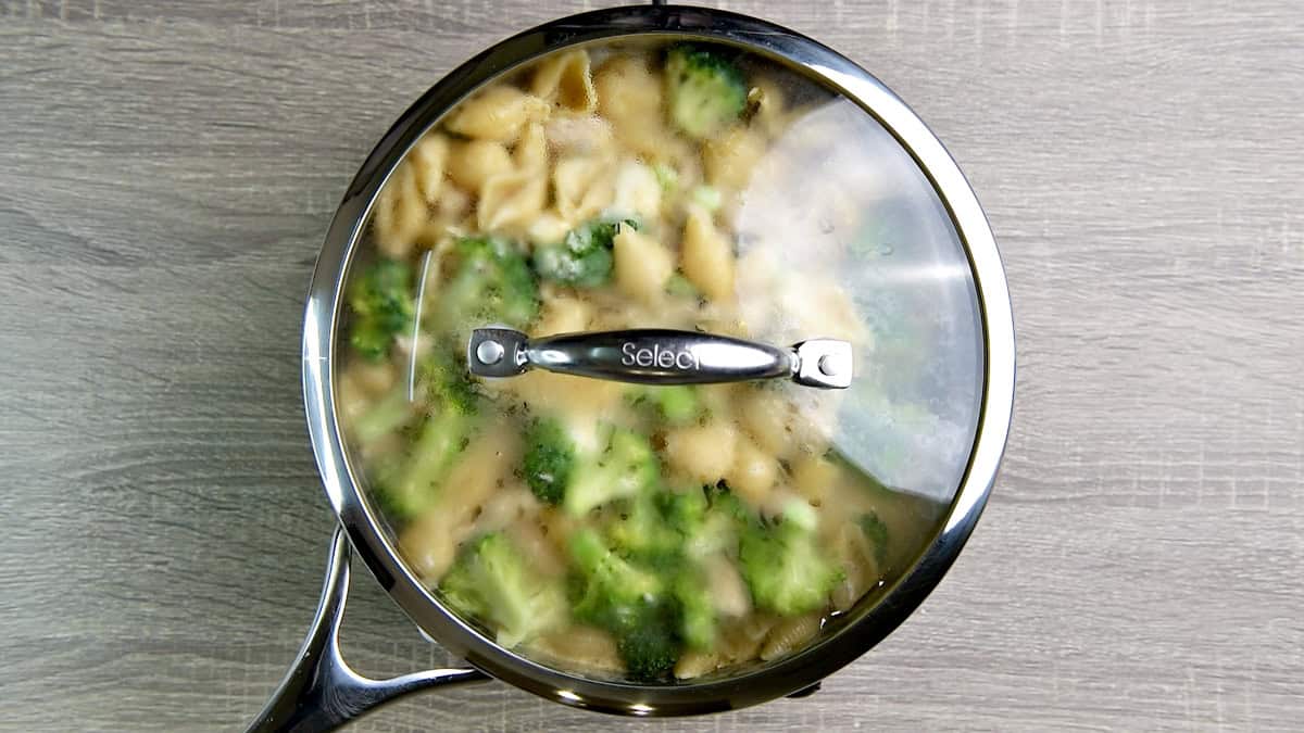 Skillet with pasta, broccoli, and chicken covered with the lid.