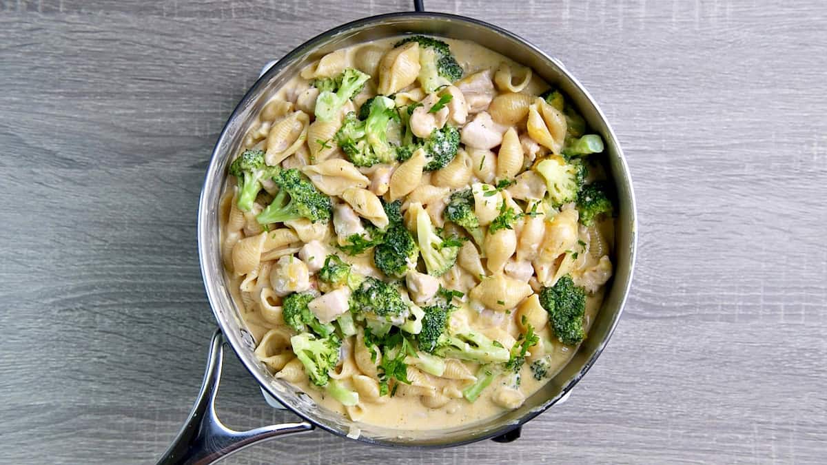 Deep skillet with cooked chicken broccoli pasta in a cheese sauce.