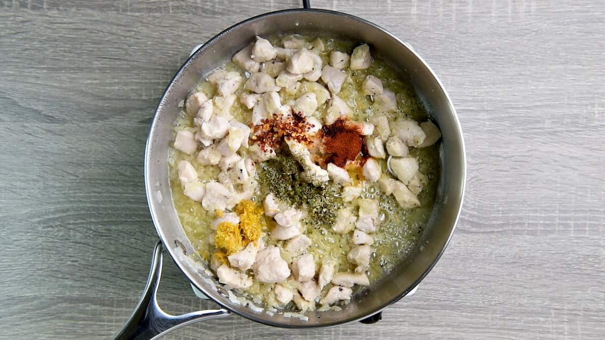 Cooked chicken in a skillet with dried seasonings and lemon zest added.