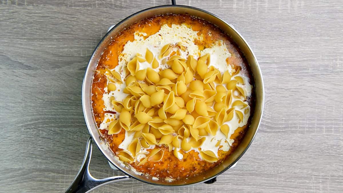 Adding pasta noodles to the pan with broth, seasoning, and heavy cream.