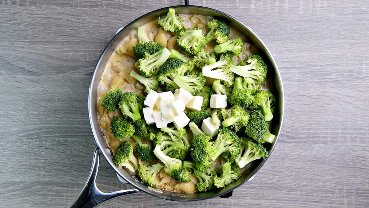 Adding cubes of cream cheese and fresh broccoli florets to the skillet.